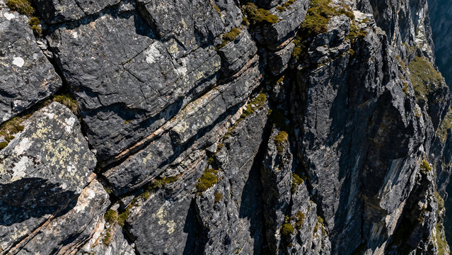 Rugged rocky cliff face with moss and lichen under bright sunlight