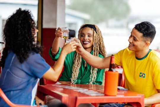Brazilian friends enjoying drinks and watching football together at a casual bar, celebrating and socializing in a vibrant atmosphere.