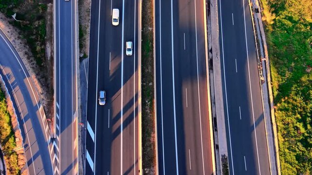 Aerial shot of a highway with white lane markings and long shadows cast across the road surface. Green grass borders the side of the road.