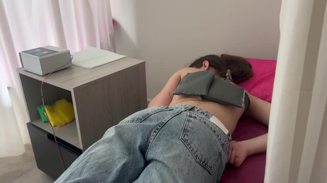 Physiotherapist placing electrodes on young female patient back