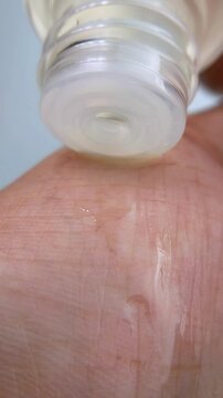 Pouring clear liquid from transparent product packaging onto hand skin. Close up view of skin being moisturized with hydrating cream, fresh skincare concept on clean background.