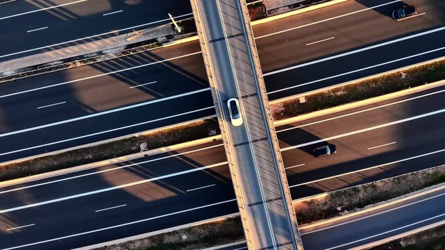 Aerial top down view of a highway and overpass during late afternoon. Long shadows stretch across the asphalt. Highway lanes and bridge with cars