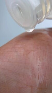 Clear liquid droplets dripping onto hand skin, looking shiny and glossy like oil. Cleansing concept for beauty, fresh skincare hydration and daily routine on clean background.