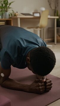 Vertical shot of young adult Black man exercising in low plank position while CGM device on upper arm tracking blood sugar level during home fitness routine