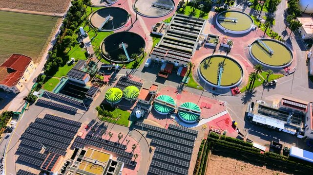 Water treatment station components including filtration tanks, solar modules, and industrial buildings. Overhead view of circular clarifiers and solar power panels