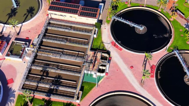 Technical aerial shot of sewage treatment architecture featuring rectangular biological basins and circular secondary clarifiers. Rectangular filtration basins and circular clarifier tank overhead.