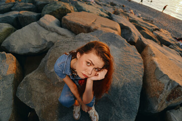 Fototapeta premium lifestyle woman in modern boho-western denim street style sits on rocks with thoughtful expression, natural light and film color enhancing vintage vibe