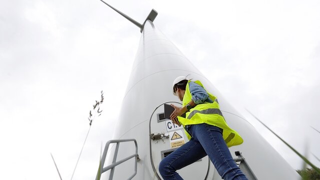 Female engineer inspecting a modern wind turbine, focusing on green energy, sustainability, and renewable resource management, ensuring efficient power generation and environmental protection