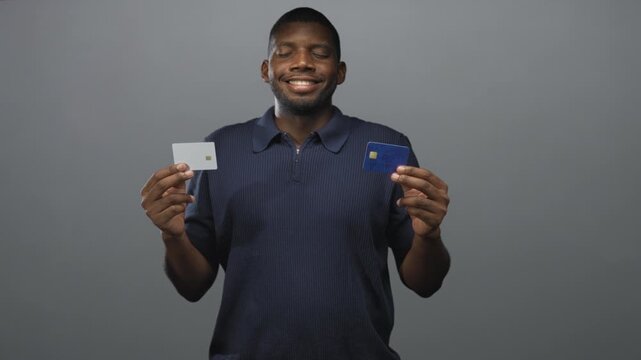 Man holding two credit cards in hands while smiling with closed eyes in studio; financial decision confidence.