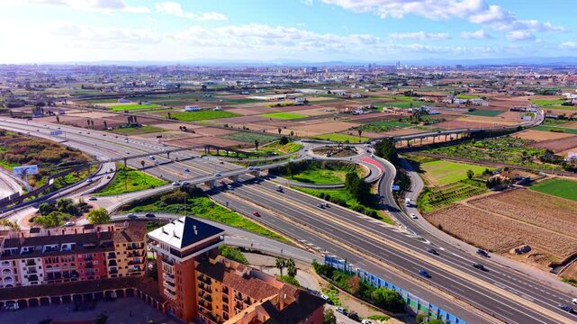 Wide landscape a large road intersection surrounded by farm land and distant city horizon. Panoramic aerial view of highway through agricultural fields.