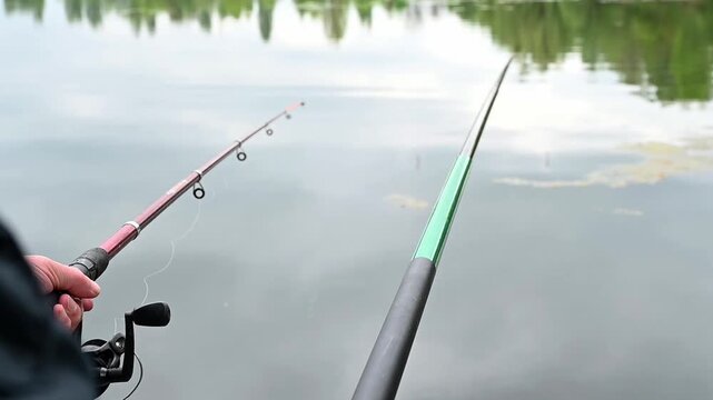 Two fishing rods are set at a calm lake in the early morning with reflections on the water and a hint of nature around