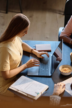 Vertical shot of young adult Caucasian woman typing on laptop during team meeting, reviewing documents and notes. Suitable for business planning, collaboration, remote work content