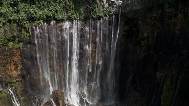Majestic Tumpak Sewu Waterfall cascading down a lush green cliff face in tropical East Java