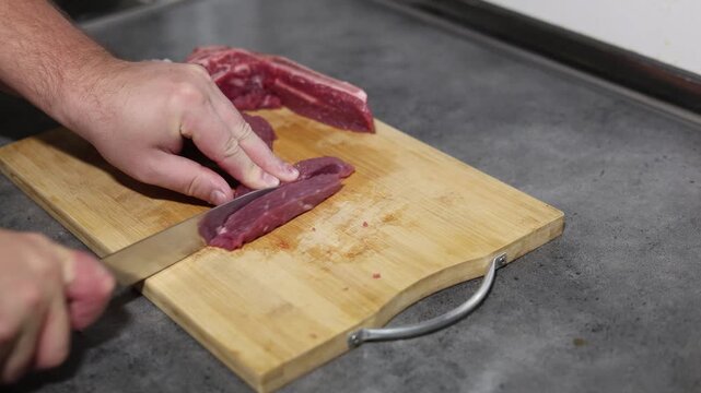 Horizontal 4K top view video. Male hand cutting piece of raw fresh juicy beef meat with knife on wooden cutting board on kitchen table. Concept of preparing dinner, healthy food, no vegan cafe, lunch