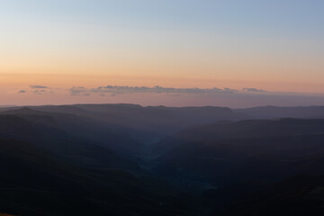 Fototapeta premium Wide panoramic sunset landscape from Bermamyt Plateau, Karachay-Cherkess Republic, Russia, with soft pastel sky and layered mountain ridges fading into haze