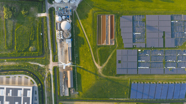 Aerial view of the Wabico BV renewable energy facility featuring solar panel arrays, a wind turbine, and industrial tanks surrounded by green fields in Waalwijk, Noord-Brabant, Netherlands.