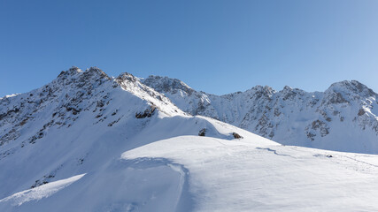Panoramic view of snow-covered mountain ridge and ski terrain near Karakol ski base, Issyk-Kul Region, Kyrgyzstan, under clear blue sky on a sunny day © TravelFlow