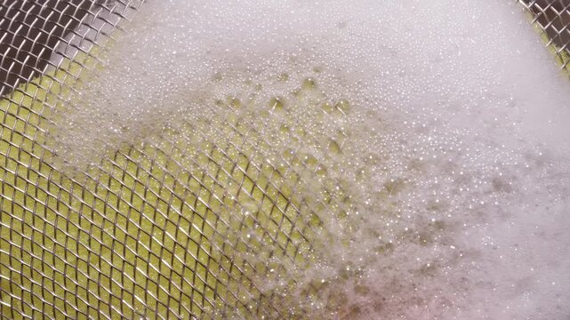 Foam Covered Metal Mesh Strainer with Yellow Cleaning Sponge Texture in Kitchen Sink, Macro Top View Slider Shot, Slow Motion Hygiene Concept and Washing Process