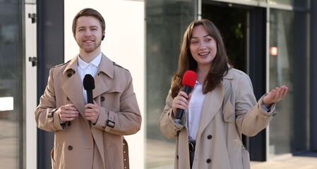 Professional journalists with microphones working on city street