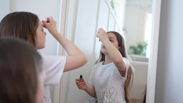 Girls applying mascara and lipstick happily in front of mirror in airy white bedroom. Blush, lipstick, mirror, girls, happy, white, bedroom.