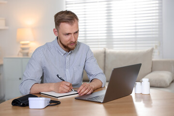 Fototapeta premium Telemedicine. Man having online consultation with doctor via laptop at wooden table indoors