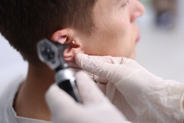 Fototapeta premium Hearing test. Doctor examining man's ear with otoscope in clinic, closeup