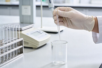 Scientist carefully adds liquid drop to beaker using pipette in a sterile laboratory setting © Snide12
