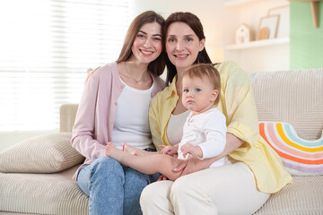 Fototapeta premium LGBT parents. Happy lesbian couple with their cute baby on sofa at home