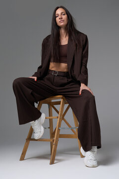 Woman in brown pinstripe suit sitting on wooden ladder stool in studio