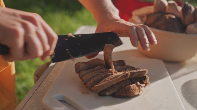 Caucasian hands slicing grilled meat campsite in warm afternoon sun, sharp knife and chopping board next to portable stove and bowl, quick rhythmic cuts for sandwiches and camp plates, energetic
