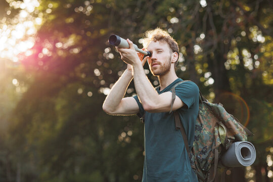 Young man has a spyglass while standing in a forest at summer