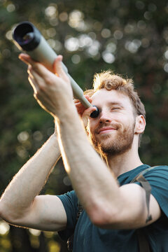Young man has a spyglass while standing in a forest at summer