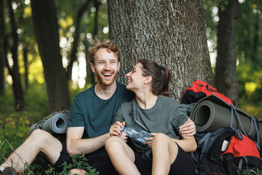 Photo of couple sitting in forest at summer with backpacks
