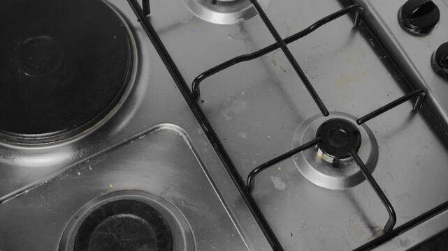 Person removing a black iron grate from a dirty stainless steel stove top