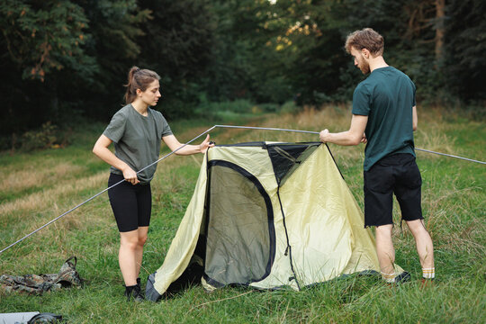 Young couple setting up a tent in forest at summer
