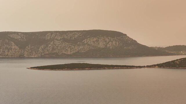Cinematic drone flyby from left to right along the coastline near Ermioni Greece, showcasing calm sea and dramatic Sahara dust sky