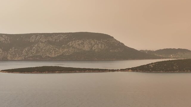 Drone flyby along the coastline from right to left near Ermioni Greece, cinematic Mediterranean landscape and calm sea under orange sky