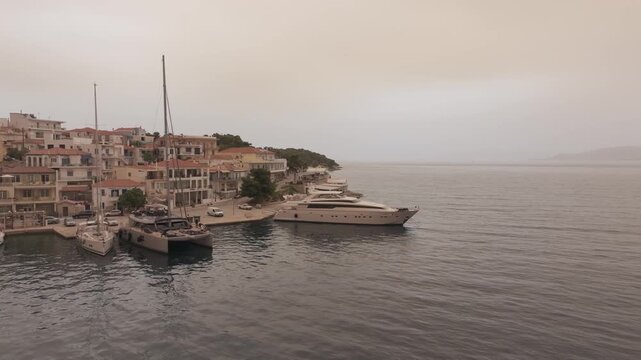 Cinematic drone orbit left to right around luxury yacht docked in Ermioni marina under surreal orange Sahara dust sky in Greece