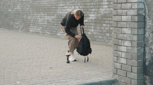 Teen inspecting phone and gear. Youthful person analyzing equipment while strolling along brick wall. Young adventurer equipped with camera and backpack walking purposefully toward railway station