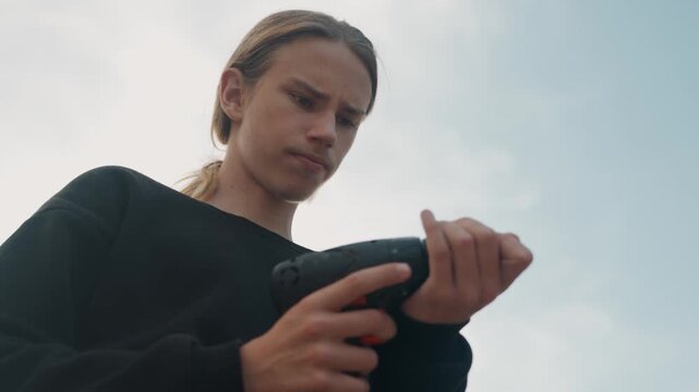 White teen inspecting cordless drill outdoors, apprentice carpenter checks battery and chuck in lowangle cinematic shot, soft sky backdrop, focused expression, hands adjusting bit, careful prep