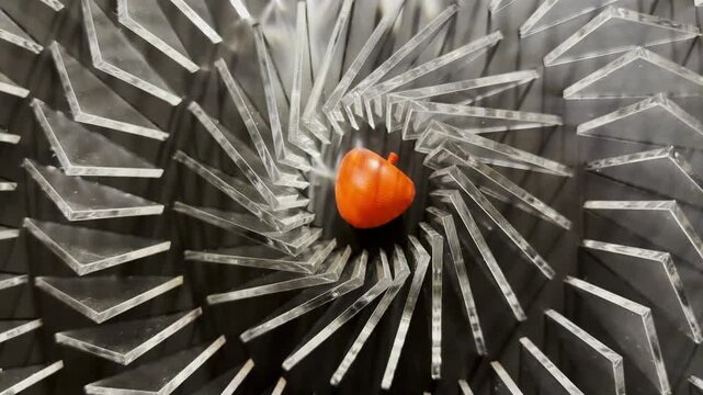 Top view on spiral geometric installation with metallic radial elements surrounding a red apple-shaped object in the center. Strong symmetry, depth and optical movement create a striking visual focus