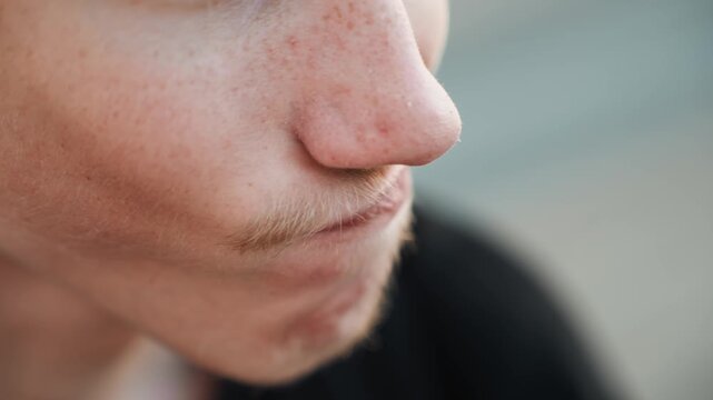 Closeup young man skater smirking during street practice, subtle grin with mustache and stubble, soft bokeh background, daylight mood conveying youthful playful energy and candid charm