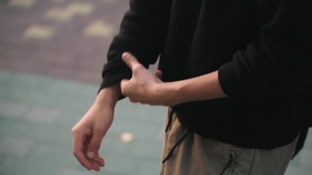 Closeup caucasian hands wet with raindrops adjusting sleeve. Damp pavement setting with muted tones frames show rolling cuffs, steadying forearm, quick grip and steady breath, commuter or artist