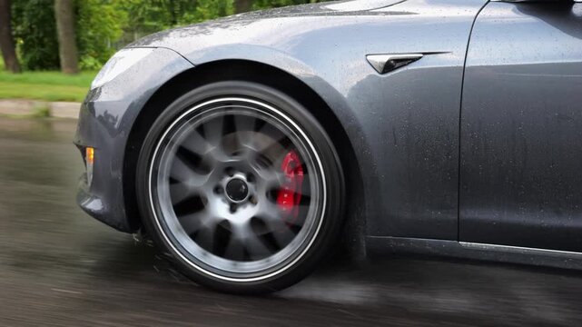 Wheel of modern electrical automobile driving at urban road on rainy day. Ecology friendly car riding moving along motorway. Electric vehicle riding through empty highway. Green innovation concept