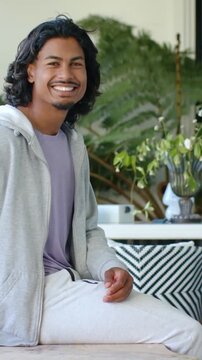 Vertical video: Smiling man shifting hands on bench for ease with frame tightening, in gray hoodie