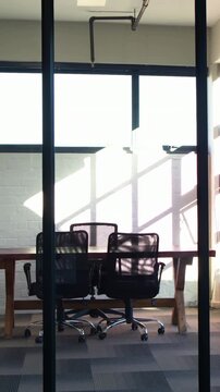 Vertical video: Sliding camera centering trestle table and two chairs in office showing shadows