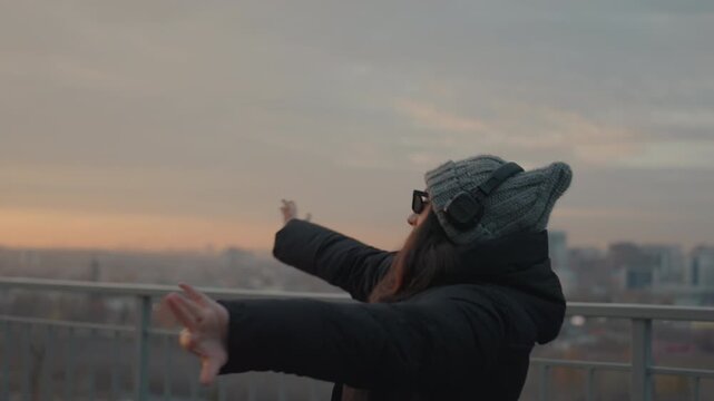 Dancer at sunset. Woman in sunglasses performs artistic dance with sunset scenery behind. Choreographed female dancer in stylish attire showcases expressive movements at evening sunset backdrop