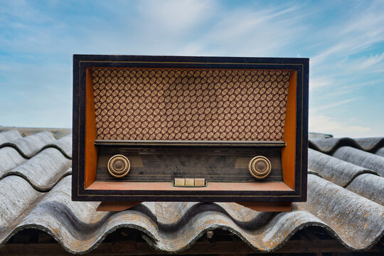 Vintage Tube Radio Placed on a Corrugated Rooftop Against the Sky with light clouds.