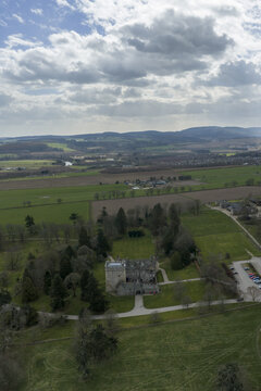Aerial view of Drum Castle featuring its historic stone tower, lush green estate, and rolling Scottish countryside under a dramatic cloudy sky Drumoak, Scotland, United Kingdom.
