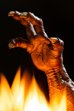 A scary demon hand reaches upward through orange flames, conveying horror, danger and supernatural terror. Dramatic lighting highlights charred skin and claws. Ideal for Halloween and spooky designs.